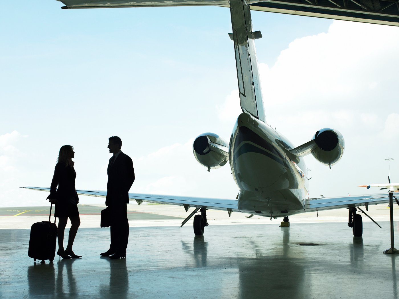 Two business travellers talking beside a private jet in a hangar